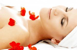 Woman lying down with hair in towel covered in red petals.