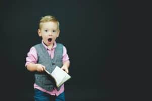 Child with a book and a shocked expression on his face.