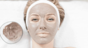 Woman wearing brown face mask next to bowl of brown substance.