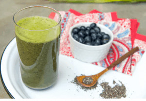 Glass of green juice on plate with berries and chia seeds.