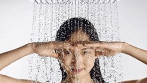 Woman under running shower head with her hands shading her eyes. 