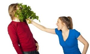 Woman putting bouquet of herbs in man's face.