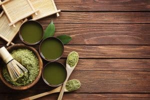 Green powder is bowl with green liquid in three bowls on wooden table.