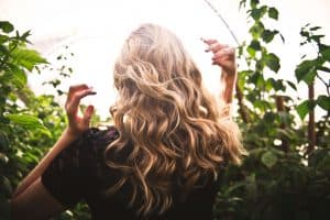 Back of blonde-haired woman in greenery.