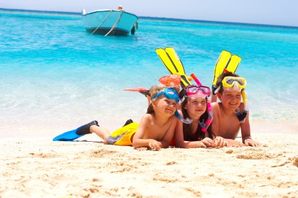Three children wearing snorkeling gear on the beach.