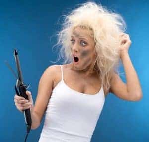 Blond-haired woman with messy hair and soot on her face surprised by a curling iron. 