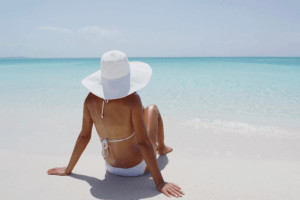 Woman in bikini sitting on beach looking at water.