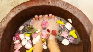 Woman soaking feet in tub of water and petals. 