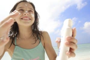 Girl applying sunscreen on beach.