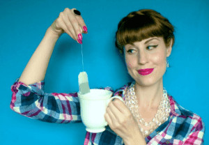 Woman holding tea bag over tea cup.