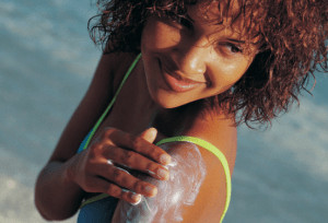 Woman on beach applying sunscreen to her arm. 