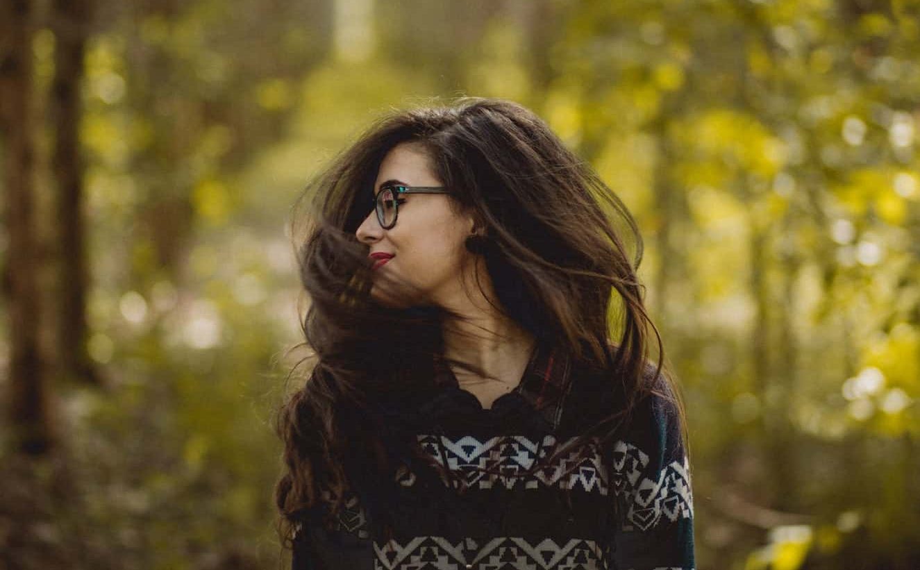 Woman flipping hair while surrounded by trees. 