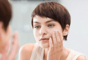 Woman applying cream to face.