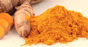 Powdered turmeric next to whole plant.