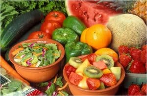 Bowl of salad and bowl of fruit surrounded with fruits and vegetables.