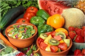 Bowl of salad and bowl of fruit surrounded with fruits and vegetables. 