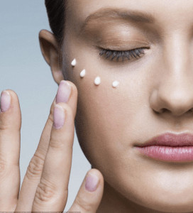 Woman dabbing row of lotion drops on her face.