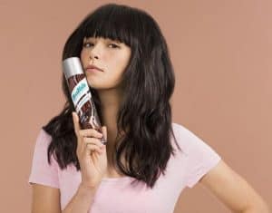 Brunette woman holding a can of batiste dry shampoo.