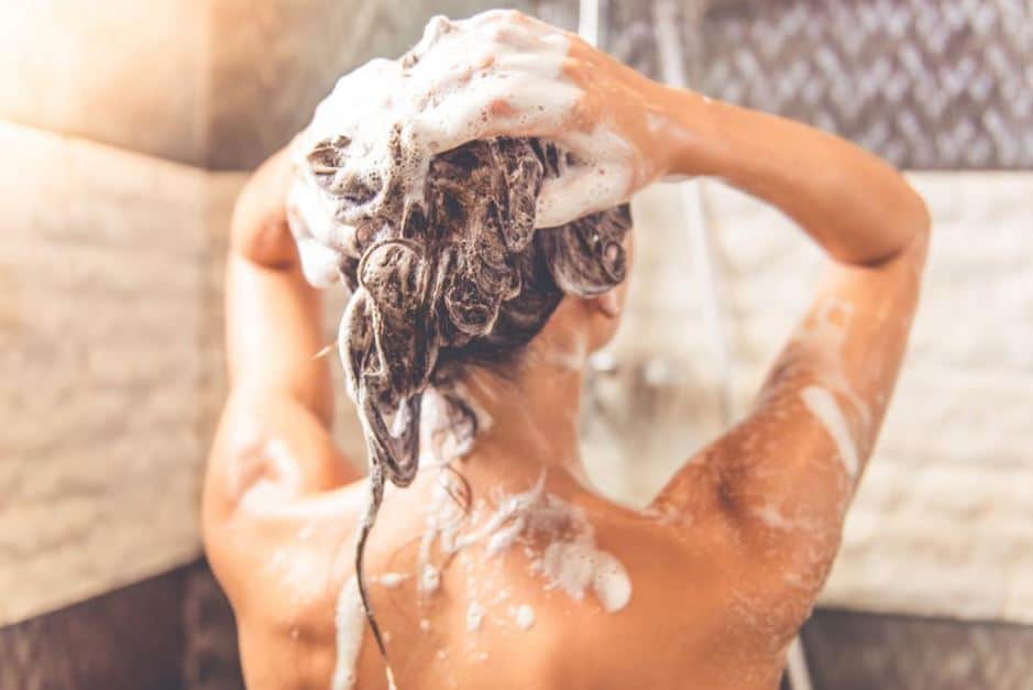 Brunette woman shampooing her hair while showering.