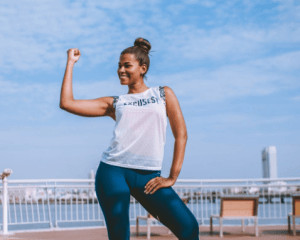 Woman on seafront holding her arm up to show muscles. 