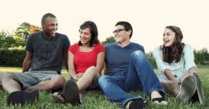 Friends sitting on grass and smiling. 