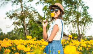 Woman standing in field of flowers and smelling a flower. 