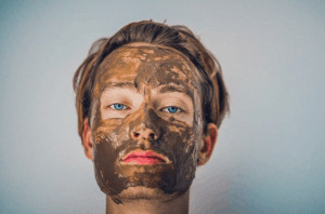 Woman with clay face mask on grey background.