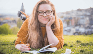 Woman laying on grass smiling with a notebook open. 