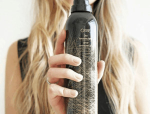 Close up of woman holding Oribe texturizing spray.