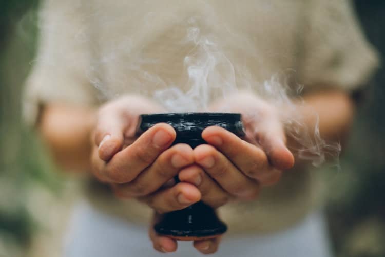 Woman hands holding small bowl that has smoke coming out.