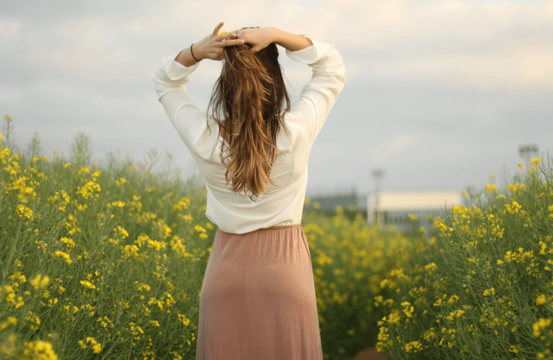 Back view of woman in field holding her hair up.