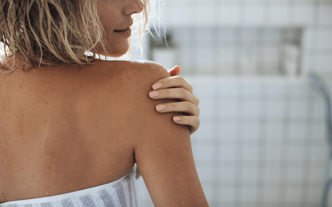 Back view of woman applying moisturizing lotion to skin.