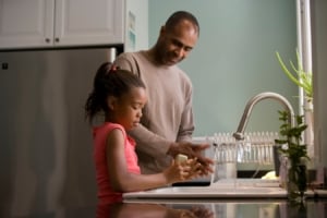 Dad washing hands with his daughter by the sink.