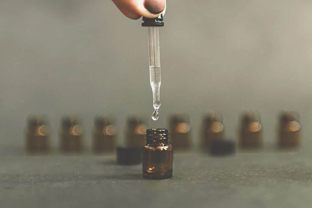 Hand dropping oil into bottle with row of bottles in background.